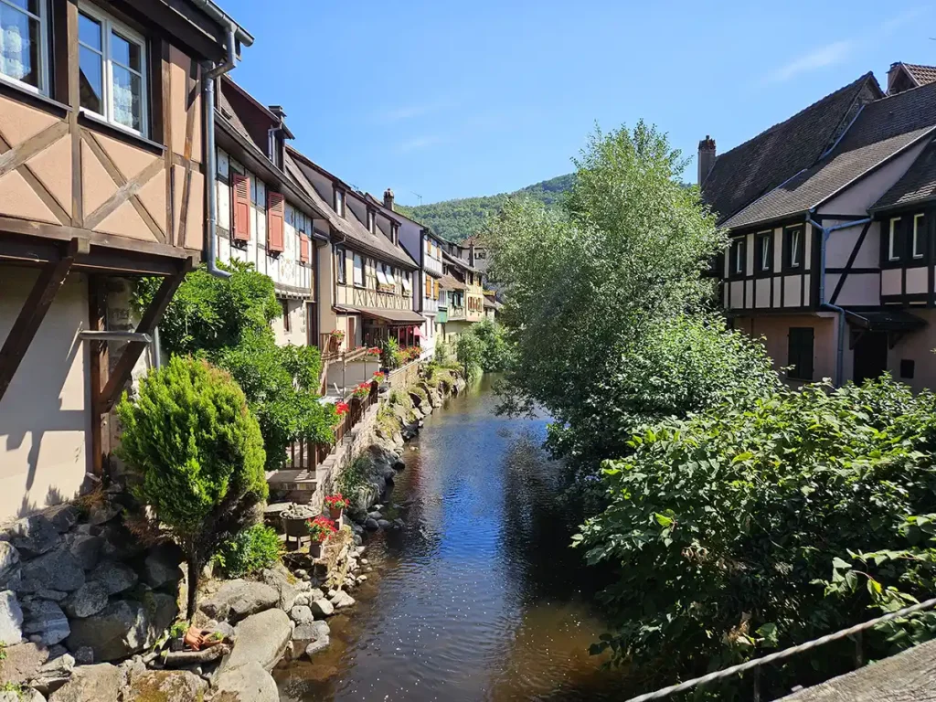 A peaceful stream flowing between traditional half-timbered houses in Kaysersberg, Alsace.